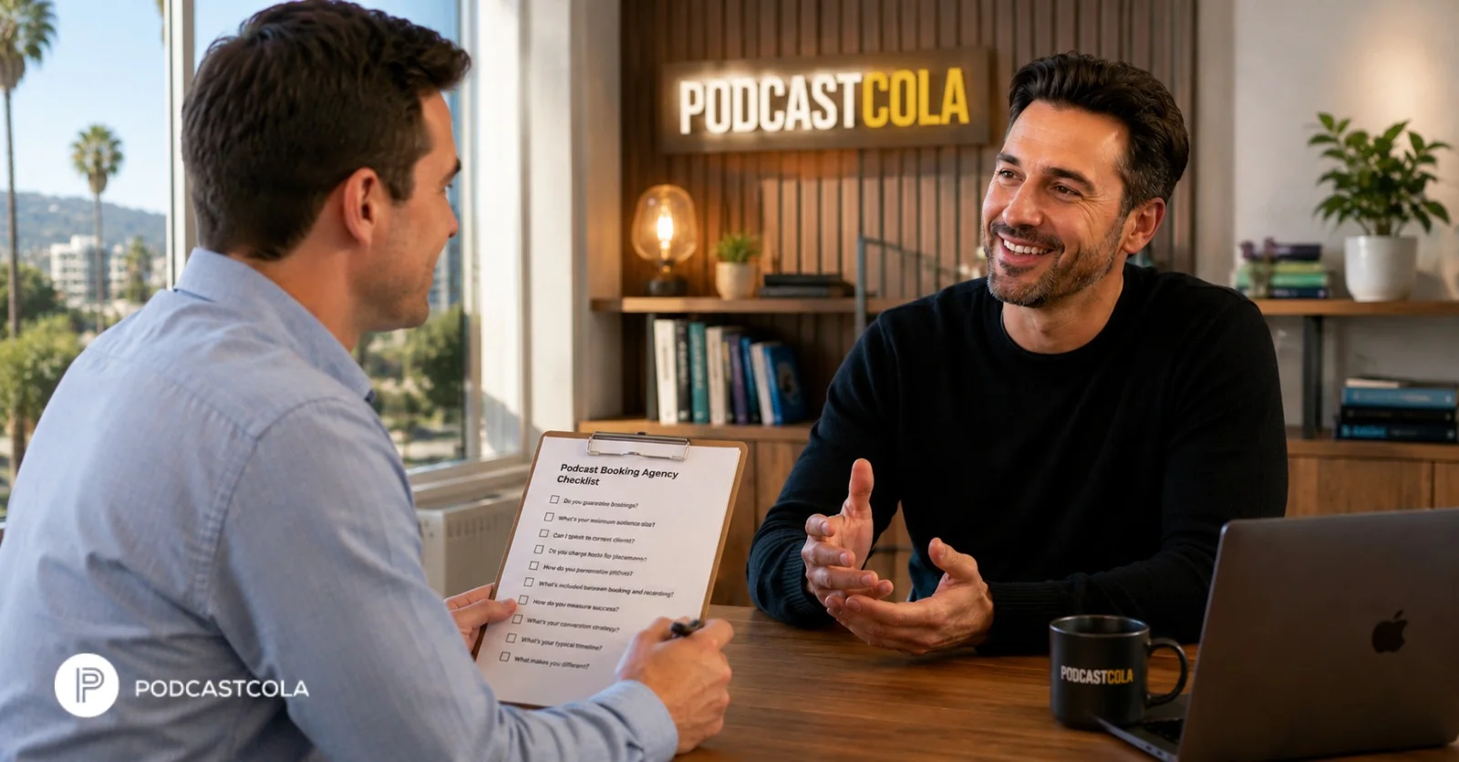 Two professional men smiling and having a conversational meeting in an office setting with a "PodcastCola" sign in the background, representing a Podcast Booking Agency at work.